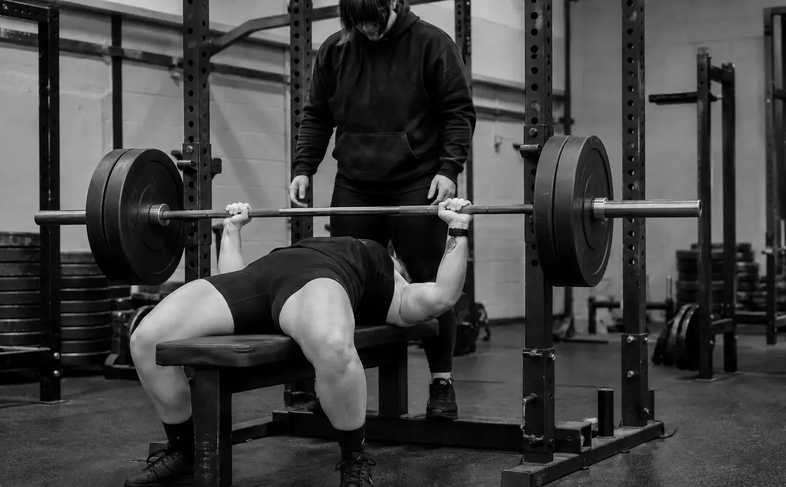 A woman bench pressing with a coach spotting