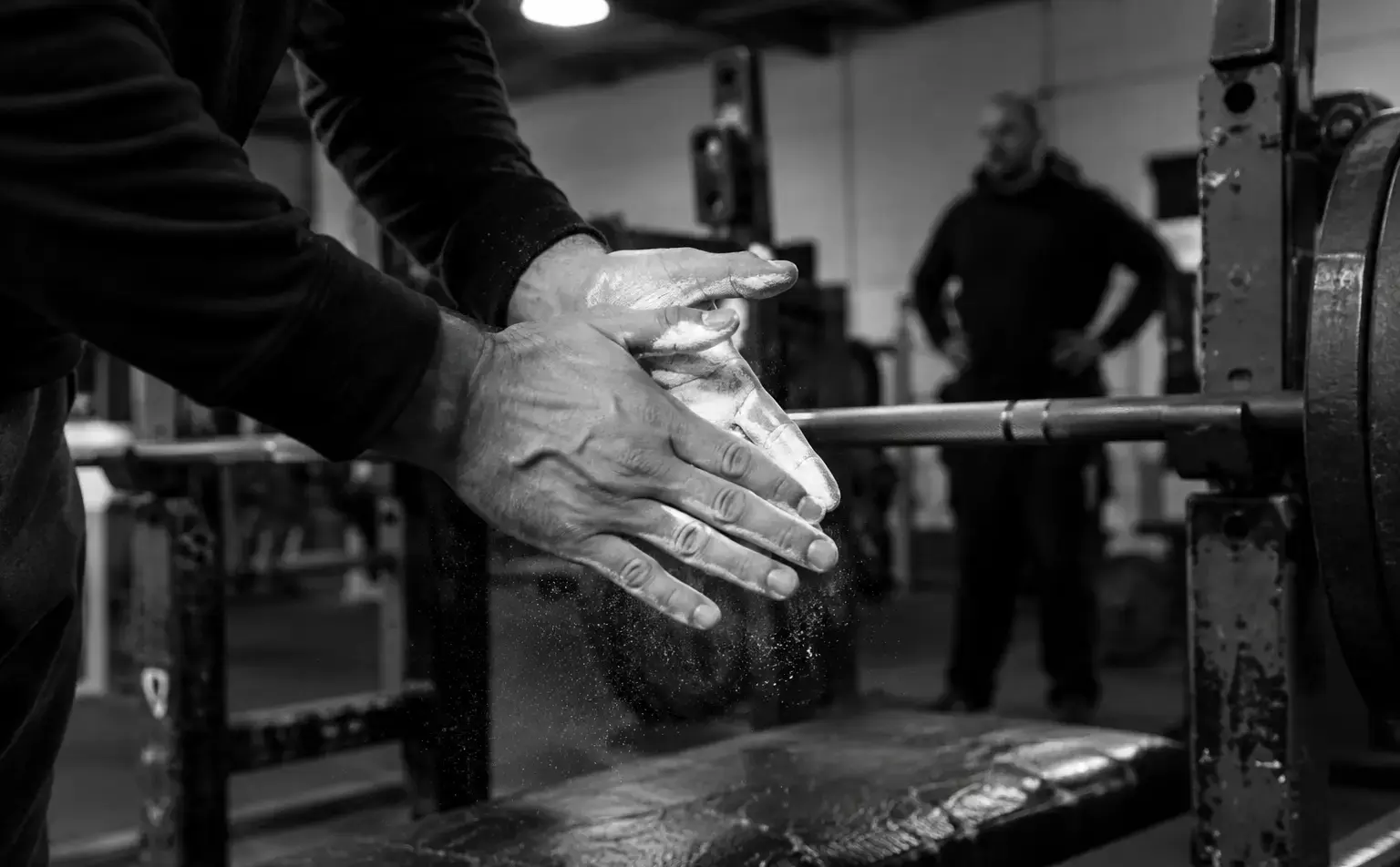 A lifter chalking their hands beside a barbell in a strength gym