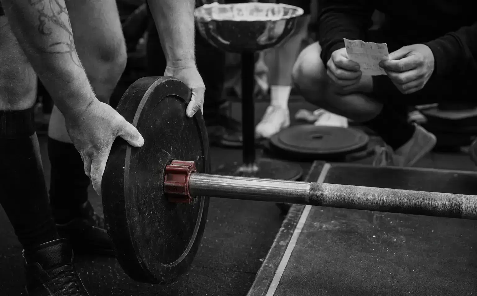 A powerlifting bar being loaded while an attempt card is checked